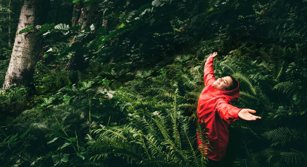 Mujer en el bosque con los brazos abiertos, sonriendo hacia el cielo